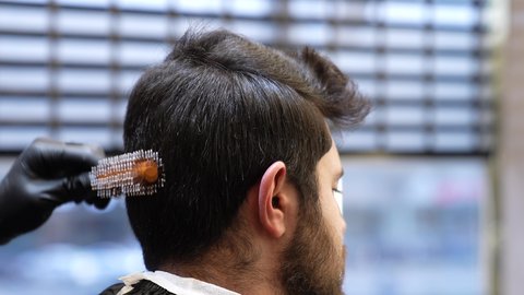 المحافظة على الأناقة والنظافة الشخصية، صالون تجميلي رجالي لتصفيف الشعر, تقديم خدمات العناية الشخصية، ممارسة مهنه الحلاقة, تصوير مقرب ليد حلاق عربي خليجي سعودي يقوم بتمشيط شعر الزبون باستخدام الفرشاة