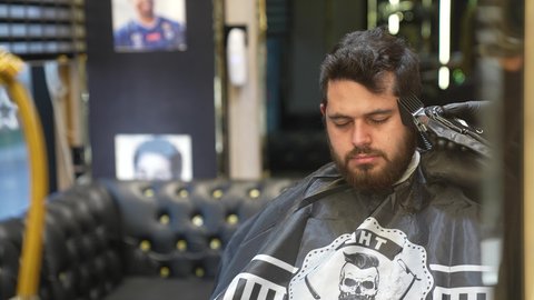 تصفيف الشعر والعناية بمظهره , تقديم خدمات العناية الشخصية، الممارسة مهنه الحلاقة, تصوير مقرب ليد حلاق عربي خليجي سعودي يقوم بحلاقة شعر الزبون باستخدام ماكينه الحلاقة