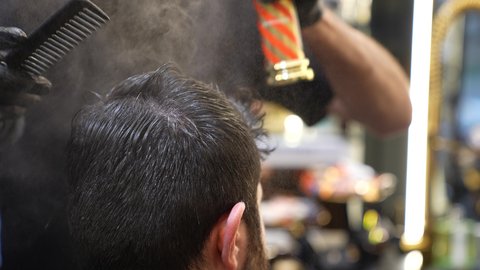 روتين العناية بالشعر , تقديم خدمات العناية الشخصية، الممارسة مهنه الحلاقة, تصوير مقرب ليد حلاق عربي خليجي سعودي يقوم برش سبراي مثبت الشعر للزبون