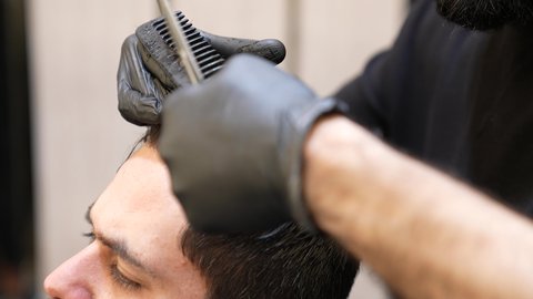 المحافظة على شعر صحي وأنيق ،استعمال ادوات المقص و المشط, تقديم خدمات العناية الشخصية، الممارسة مهنه الحلاقة, تصوير مقرب ليد حلاق عربي خليجي سعودي يقوم بحلاقة شعر الزبون