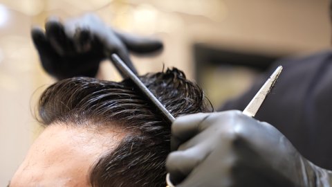 استعمال ادوات المقص و المشط, تقديم خدمات العناية الشخصية، الاهتمام بالشكل الخارجي، الممارسة مهنه الحلاقة, تصوير مقرب ليد حلاق عربي خليجي سعودي يقوم بحلاقة شعر الزبون