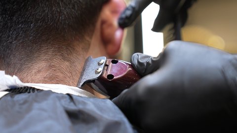 استخدام الغطاء الاسود لحماية الملابس، استعمال ماكينة الحلاقة, تقديم خدمات العناية الشخصية، الاهتمام بالشكل الخارجي، الممارسة مهنه الحلاقة, تصوير مقرب ليد حلاق عربي خليجي سعودي يقوم بحلاقة ذقن الزبون