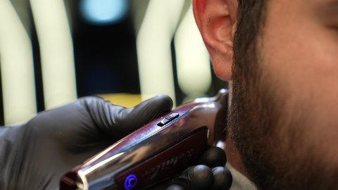 استعمال ماكينة الحلاقة, تقديم خدمات العناية الشخصية، الاهتمام بالشكل الخارجي، الممارسة مهنه الحلاقة, تصوير مقرب ليد حلاق عربي خليجي سعودي يقوم بحلاقة ذقن الزبون