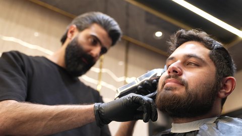 جلسة تجميل وعناية شخصية، الممارسة مهنه الحلاقة، تقديم خدمات العناية الشخصية, تصويرمقرب لحلاق عربي خليجي سعودي  يقوم بقص شعر الزبون باستخدام ماكينه الحلاقة