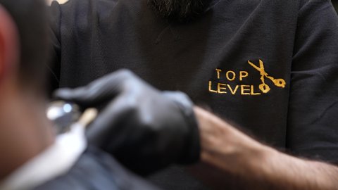 جلسة حلاقة شعر وتهذيب لحية، الممارسة مهنه الحلاقة، تقديم خدمات العناية الشخصية, تصويرمقرب ليد حلاق عربي خليجي سعودي  يقوم بقص شعر الزبون باستخدام ماكينه الحلاقة