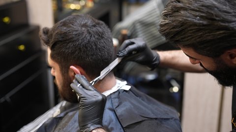 صالون حلاقة لقص و تصفيف الشعر للرجال، الممارسة مهنه الحلاقة، تقديم خدمات العناية الشخصية, تصويرمقرب لحلاق عربي خليجي سعودي يرتدي يونيفورم الصالون يقوم بقص شعر الزبون