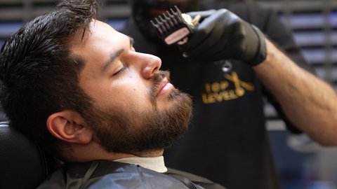 استخدام أدوات و معدات الحلاقة، استعمال ماكينة الحلاقة لتحديد الذقن، المحافظة على الأناقة والنظافة الشخصية، تقديم خدمات العناية الشخصية, تصويرمقرب ليد حلاق عربي خليجي سعودي يقوم بالحلاقة للزبون، صالون تجميلي رجالي