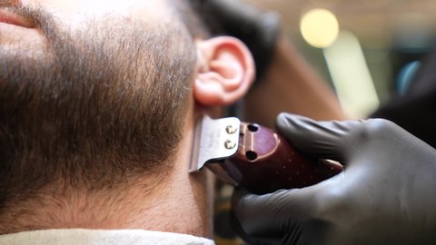 استعمال ماكينة الحلاقة لتحديد الذقن، المحافظة على الأناقة والنظافة الشخصية، تقديم خدمات العناية الشخصية, تصويرمقرب ليد حلاق عربي خليجي سعودي يقوم بالحلاقة للزبون، صالون تجميلي رجالي