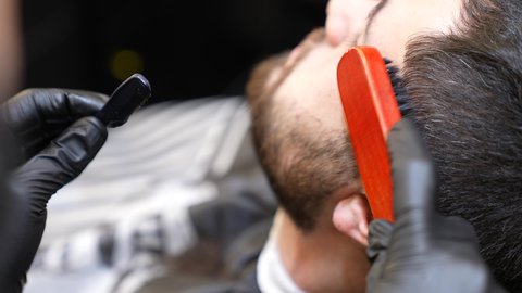 العناية بالبشرة والاهتمام بالمظهر الخارجي، تصوير مقرب ليد حلاق عربي خليجي سعودي يقوم بإزالة شعر الوجه باستخدام شفرة الحلاقة الرجالية للزبون، مفهوم العناية بالبشرة والنظافة الشخصية