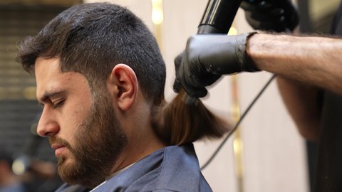 Maintaining elegance and personal hygiene, skin care and attention to one's appearance, a close-up of a Saudi Arabian Gulf barber's hand using an electric hair dryer (hair dryer) for the customer, maintaining healthy and elegant hair