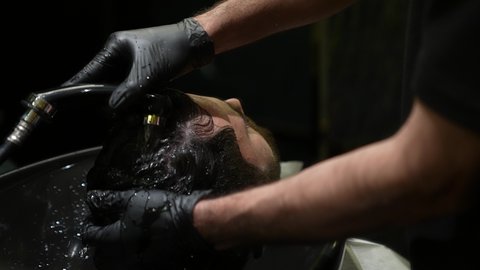 صالون تجميلي رجالي لتصفيف الشعر، العناية والإهتمام بشعر صحي ونظيف، ممارسة مهنة الحلاقة, تقديم خدمات العناية الشخصية, الاهتمام بالشعر و النظافة البدنية، تصوير مقرب ليد حلاق عربي خليجي سعودي يقوم بغسيل شعر الزبون