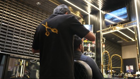 تقديم خدمات العناية الشخصية، العناية والاهتمام بالجمال والأناقة والمظهر الخارجي، المحافظة على شعر صحي وأنيق، تصويرمقرب من الخلف لحلاق عربي خليجي سعودي يرتدي زي الحلاقين التقليدي يقوم بتصفيف شعر الزبون، روتين العناية بالشعر