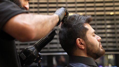 Care and attention to beauty, elegance and appearance, maintaining healthy and elegant hair, close-up of a Saudi Arabian Gulf barber blow-drying a customer's hair, hair care routine, providing personal care services