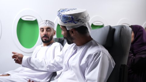 Pinpointing a specific location, pointing to something, close-up of two Arab Gulf Omani friends sitting on airplane seats on a flight, one of them pointing somewhere with his index finger.