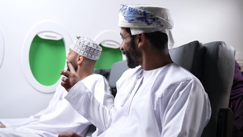 الاشاره الى شئ ما ،تحديد موقع معين، تصوير مقرب لصديقان عربيان خليجيان عمانيان يجلسان على كراسي الطائره في رحله جويه ، احداهما يشير باصبع السبابة الى مكان ما