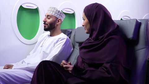 Pointing to something, specifying a specific location, close-up of an Arab Gulf Omani couple sitting on airplane seats on a flight, one of them pointing their index finger somewhere.