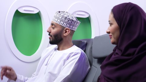Pointing to a specific location, pointing to something, close-up of an Arab Gulf Omani couple sitting on airplane seats on a flight, one of them pointing their index finger somewhere.