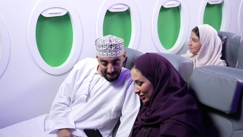 الترفيه والتسليه وقضاء الاوقات داخل الطائره ، التقاط صور السيلفي ،  دمج التقنيات فى الحياه اليوميه ، تصوير مقرب لرجل وامرأه عربييان خليجييان عمانييان يجلسان على كراسي الطائره في رحله جويه