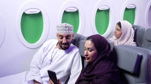 التقاط صور السيلفي ، الترفيه والتسليه وقضاء الاوقات داخل الطائره ،دمج التقنيات فى الحياه اليوميه ، تصوير مقرب لرجل وامرأه عربييان خليجييان عمانييان يجلسان على كراسي الطائره في رحله جويه