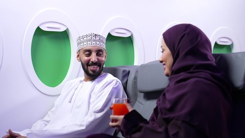 شرب المشروبات الباردة ، الحوار وتبادل الاحاديث بين افراد الاسرة، الترفيه والتسليه وقضاء الاوقات داخل الطائره ،دمج التقنيات فى الحياه اليوميه ، تصوير مقرب لرجل وامرأه عربييان خليجييان عمانييان يجلسان على كراسي الطائره في رحله جويه