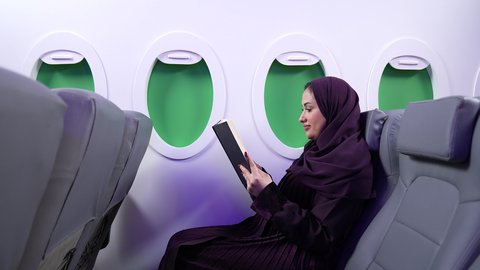 الترفيه والتسليه وقضاء الاوقات داخل الطائره ،الاستمتاع بالقراءه والثقافه ، سيدة سعودية تمارس الهوايات المفضله,  امرأه عربيه خليجيه عمانيه ترتدي العباءة والحجاب تجلس على كرسي الطائره في رحله جويه