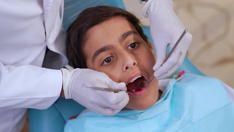 ايدي طبيب عربي خليجي عماني يرتدي القفازات الطبية يقوم بفحص أسنان المريض، الادوات اللازمة لإجراء الفحوصات، معالجة النخر والتسوس,الحصول على ابتسامة مثالية، تصوير مقرب لولد عربي خليجي عماني يرتدي الزي التقليدي يجلس في العيادة السنية ويفتح فمه لتشخيص المرض