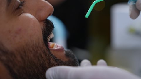 مفهوم الطب والرعاية الصحية، العناية بالصحة الفموية، استخدام الأدوات المعقمة لإجراء الفحوصات السنية، تقديم الخدمات الطبية للمرضى, تصوير مقرب لطبيب يرتدي القفازات يقوم بفحص أسنان المريض، شاب عربي خليجي عماني يرتدي الزي التقليدي يجلس على كرسي العلاج