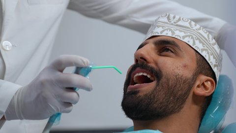 العناية بالصحة الفموية، استخدام الأدوات المعقمة لإجراء الفحوصات السنية،مفهوم الطب والرعاية الصحية، تقديم الخدمات الطبية للمرضى, تصوير مقرب لطبيب يرتدي القفازات يقوم بفحص أسنان المريض، شاب عربي خليجي عماني يرتدي الزي التقليدي يجلس على كرسي العلاج