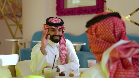 ديوانية سعودية ونقاشات وحوارات وقضاء أوقات ممتعة، محاولة التخفيف من حرارة الصيف بالمشروب المنعش، ايماءات السعادة والسرور، تصويرمقرب لرجل عربي خليجي سعودي يرتدي الثوب و الشماغ يجلس فى احدي المقاهي برفقه صديقه