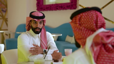 وناسة وتعارف وأجواء سعيدة في مقهى سعودي، محاولة التخفيف من حرارة الصيف بالمشروب المنعش، ايماءات السعادة والسرور، تصويرمقرب لرجل عربي خليجي سعودي يرتدي الثوب و الشماغ يجلس فى احدي المقاهي برفقه صديقه