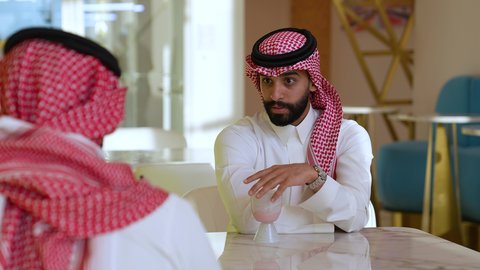 قضاء أوقات ترفيهية ممتعة، الاستمتاع بالمشروبات و الحلويات ، ايماءات السعادة والسرور، تصويرمقرب لرجل عربي خليجي سعودي يرتدي الثوب و الشماغ يجلس فى احدي المقاهي برفقه صديقة