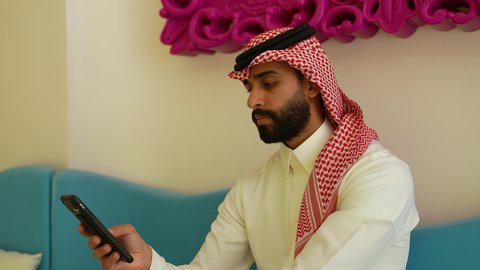 دردشات ومحادثات ودية مع الأصدقاء، الرد والإجابة على الجوال, تصوير مقرب لرجل عربي خليجي سعودي يرتدي الشماغ والثوب التقليدي يجلس فى احد المقاهي يقوم بإجراء مكالمة هاتفية عبر الهاتف المحمول, استخدام الأجهزة التقنية الحديثة