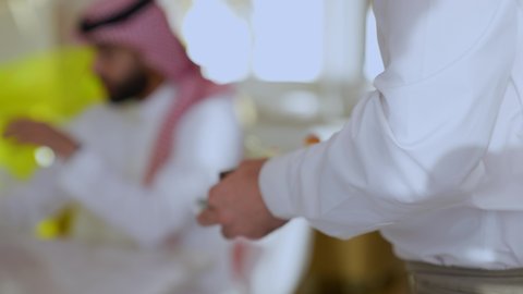 Having cold drinks and delicious sweets, having a good time outside the home, having fun and entertainment on vacation, a close-up of a Saudi Arabian Gulf man wearing a thobe and a shemagh sitting in a cafe, exchanging conversations and news