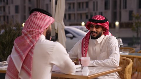 الدفع والشراء من خلال برامج وتطبيقات الجوال، تصوير مقرب لرجل عربي خليجي سعودي يرتدي الثوب و الشماغ يجلس في احدي المقهى, قضاء وقت ممتع خارج المنزل، التسلية والترفيه في العطلة