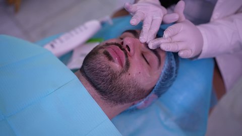 ترطيب وتنظيف وتفتيح الجلد، رجل عربي خليجي عماني يرتدي الدشداشة يجلس على كرسي العيادة ، طبيبة مختصه فى العناية بالبشرة تضع كريم المرطب على وجه الزبون ، مفهوم العناية والإهتمام بنضارة وتحسين البشرة، استخدام مكونات تجميلية شبابية