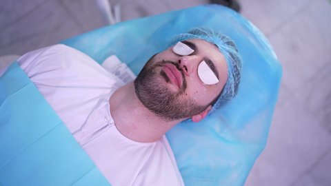 جلسات و روتين العناية بالوجه ، مفهوم الإهتمام بنضارة وتحسين البشرة،رجل عربي خليجي عماني في صالون تجميلي شبابي يضع قطع قطنية على العين ، خطوات تنظيف وتقشير وتفتيح البشرة، إستخدام مكونات تجميلية