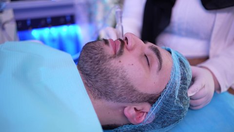 طبيبة عربية خليجية عمانية تستخدام احدث التقنيات لعلاج الوجه، تقديم الخدمات والرعاية الصحية ، جلسة ليزر في عيادة خاصة، سيد عربي عماني خليجي يجلس على كرسي العلاج في موعد بعيادة طبية مختصة بالتنظيف والعناية بالبشرة
