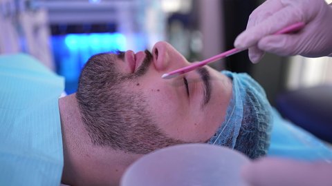 رجل عربي خليجي عماني يرتدي الدشداشة يجلس على كرسي العيادة ، طبيبة مختصه فى العناية بالبشرة تضع الماسك على وجه الزبون ، مفهوم العناية والإهتمام بنضارة وتحسين البشرة، استخدام مكونات تجميلية شبابية، ترطيب وتنظيف وتفتيح الجلد