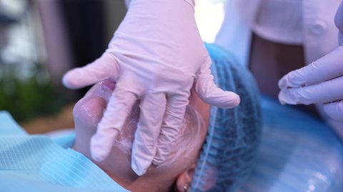 استخدام مكونات تجميلية نسائية ، مفهوم العناية والإهتمام بنضارة وتحسين البشرة، ترطيب وتنظيف وتفتيح الجلد ، سيدة عربية خليجية عمانية ترتدي العباءة تجلس على كرسي العيادة ، طبيبة مختصه فى العناية بالبشرة تضع الكريم المرطب على وجه الزبون