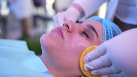 استخدام مكونات تجميلية ، ترطيب وتقشير وتفتيح الجلد، مفهوم العناية والإهتمام بنضارة وتحسين البشرة، طبيبة عربية خليجية عمانية تقوم بتنظيف الجلد باستخدام قطع اسفنجيه ، سيدة عربية خليجية عمانية ترتدي العباءة تجلس على كرسي العيادة