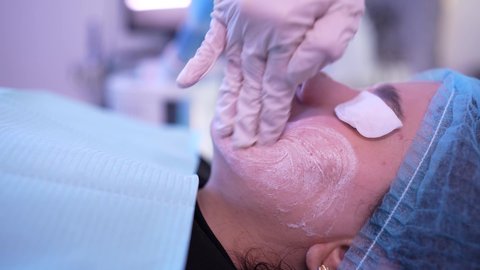 مفهوم العناية والإهتمام بنضارة وتحسين البشرة، ترطيب وتنظيف وتفتيح الجلد ، استخدام مكونات تجميلية نسائية ،سيدة عربية خليجية عمانية ترتدي العباءة تجلس على كرسي العيادة ، طبيبة مختصه فى العناية بالبشرة تضع الكريم المرطب على وجه الزبون