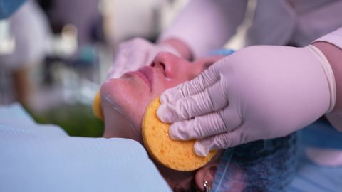 ترطيب وتقشير وتفتيح الجلد، استخدام مكونات تجميلية ، مفهوم العناية والإهتمام بنضارة وتحسين البشرة، طبيبة عربية خليجية عمانية تقوم بتنظيف الجلد باستخدام قطع اسفنجيه ، سيدة عربية خليجية عمانية ترتدي العباءة تجلس على كرسي العيادة