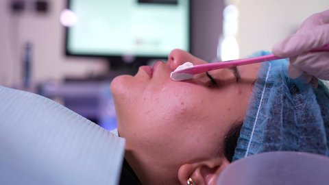 مفهوم العناية والإهتمام بنضارة وتحسين البشرة، ترطيب وتنظيف وتفتيح الجلد ، استخدام مكونات تجميلية نسائية ،سيدة عربية خليجية عمانية ترتدي العباءة تجلس على كرسي العيادة ، طبيبة مختصه فى العناية بالبشرة تضع الكريم المرطب على وجه الزبون