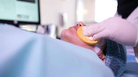 ترطيب وتقشير وتفتيح الجلد، مفهوم العناية والإهتمام بنضارة وتحسين البشرة، طبيبة عربية خليجية عمانية تقوم بتنظيف الجلد باستخدام قطع اسفنجيه ، استخدام مكونات تجميلية ، سيدة عربية خليجية عمانية ترتدي العباءة تجلس على كرسي العيادة