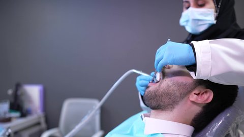المحافظة على صحة الفم والاسنان ، شاب عربي خليجي عماني يرتدي الدشداشة والكمة يجلس على كرسي العلاج في العيادة السنية ، الزيارة الدورية للاطمئنان على الصحة الفموية، معالجة النخور وتركيب الحشوات، استخدام المعدات اللازمة للجراحة ، تصوير مقرب من الجانب لطبيبة ترتدي القفازات تقوم بفحص أسنان المريض وتشخيص المرض