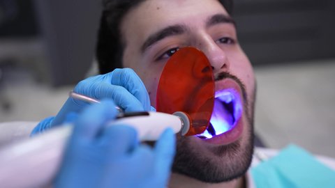 استخدام المعدات اللازمة لجراحة الاسنان ، مفهوم الطب والرعاية الصحية، تصوير مقرب من الجانب لطبيب يرتدي القفازات يقوم بفحص أسنان المريض، شاب عربي خليجي عماني يرتدي الدشداشة والكمة يجلس على كرسي العلاج في العيادة السنية، تقديم الخدمات الطبية للمرضى ، إجراء الفحوصات الدورية للعناية بالصحة الفموية