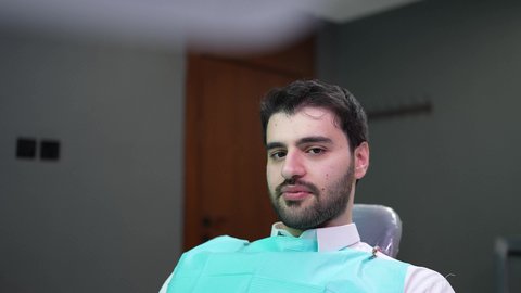 استخدام قشور فينير من الخزف لصنع ابتسامة بيضاء ناصعه، النظرإلى الكاميرا بإيماءات السعادة، مظهر انيق وجذاب ، أهمية متابعة طبيب الاسنان، العناية والتجميل والتبيض، رجل عربي خليجي عماني يرتدي الدشداشه والكمه يشير بيديه إلى أسنانه