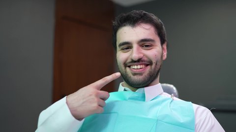 النظرإلى الكاميرا بإيماءات السعادة، مظهر انيق وجذاب ،  استخدام قشور فينير من الخزف لصنع ابتسامة بيضاء ناصعه، أهمية متابعة طبيب الاسنان، العناية والتجميل والتبيض، رجل عربي خليجي عماني يرتدي الدشداشه والكمه يشير بيديه إلى أسنانه