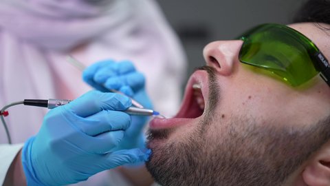 المحافظة على صحة الفم والاسنان ، الزيارة الدورية للاطمئنان على الصحة الفموية، شاب عربي خليجي عماني يرتدي الدشداشة والكمة يجلس على كرسي العلاج في العيادة السنية ، معالجة النخور وتركيب الحشوات، استخدام المعدات اللازمة للجراحة ، تصوير مقرب من الجانب لطبيبة ترتدي القفازات تقوم بفحص أسنان المريض وتشخيص المرض
