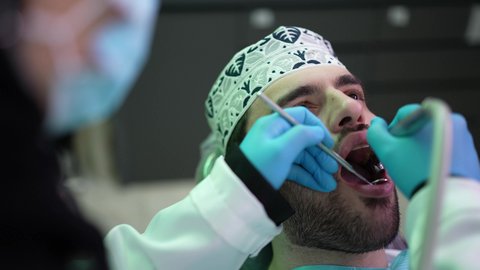 تصوير مقرب من الجانب لطبيبة ترتدي القفازات تقوم بفحص أسنان المريض وتشخيص المرض، شاب عربي خليجي عماني يرتدي الدشداشة والكمة يجلس على كرسي العلاج في العيادة السنية، الزيارة الدورية للاطمئنان على الصحة الفموية، استخدام المعدات اللازمة لجراحة الفم, معالجة النخور وتركيب الحشوات